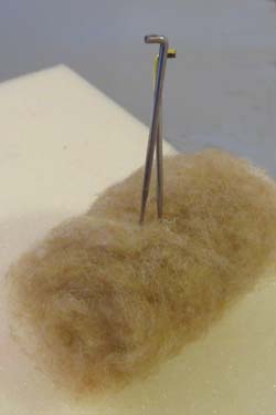Felting needles pierce a roll of wool that will become the torso of a bear.